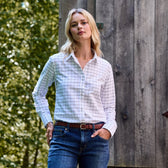 A person in a Tom Beckbe Womens Oxford Shirt and jeans stands outdoors near wood, with greenery in the background.