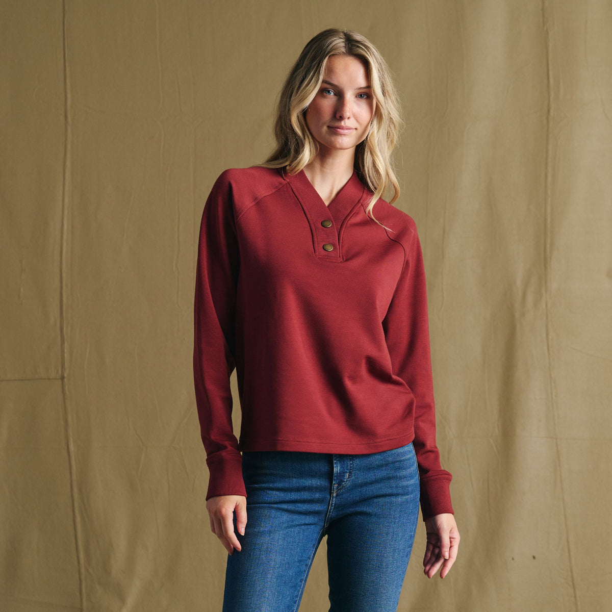 Woman in Tom Beckbe Women’s Shelby Fleece Pullover and jeans stands before tan backdrop—the perfect cool-weather layer.