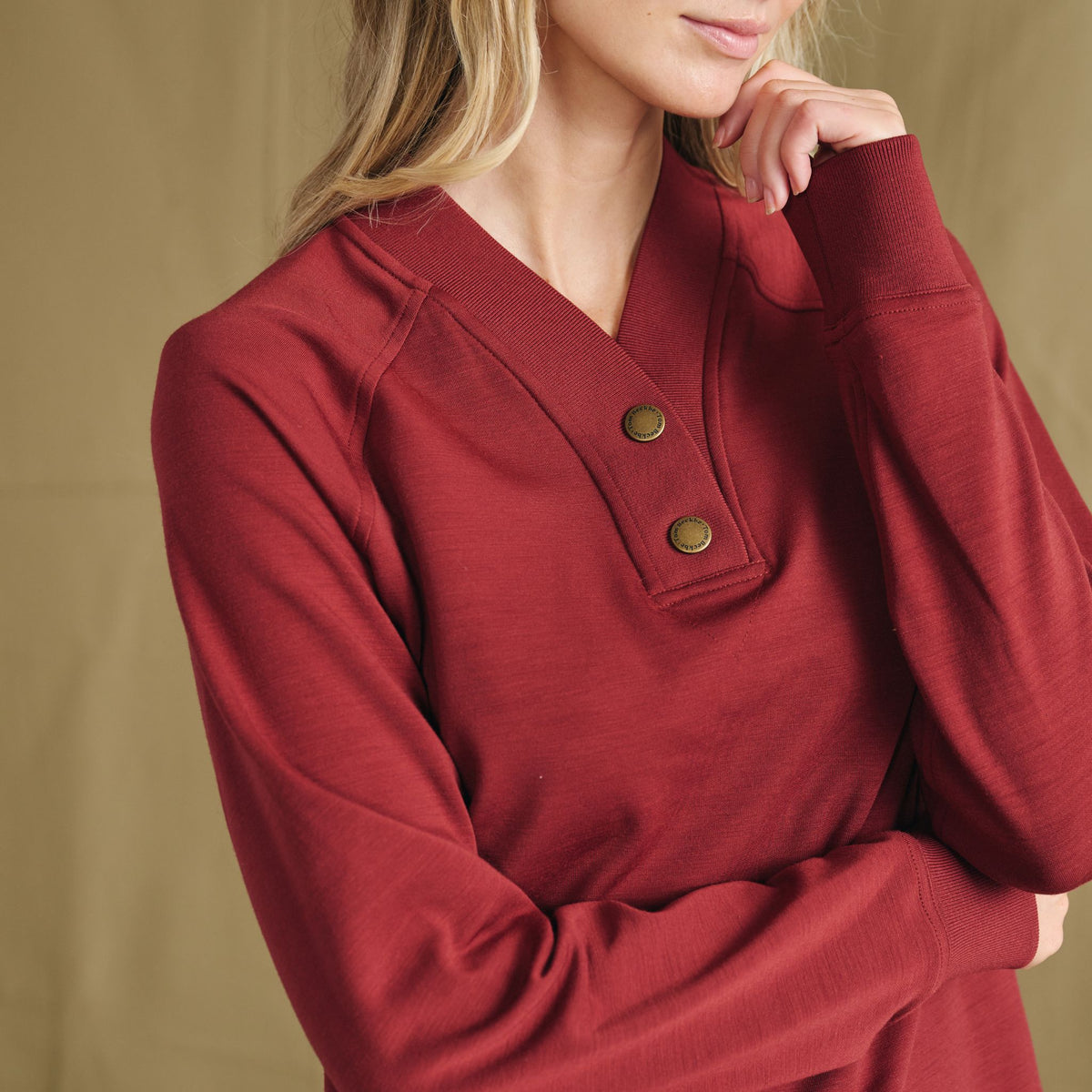 Woman in a Tom Beckbe Shelby Fleece Pullover with two buttons at the collar, standing against a tan background.