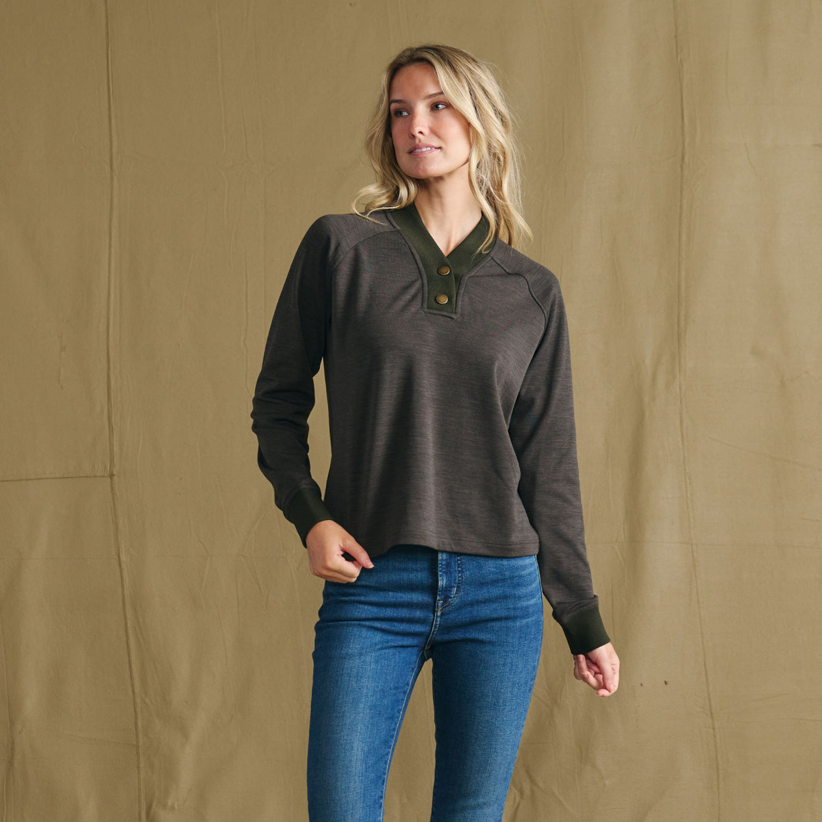 Model wears Tom Beckbe Women’s Shelby Fleece Pullover in dark long-sleeve, styled with jeans before a beige backdrop.