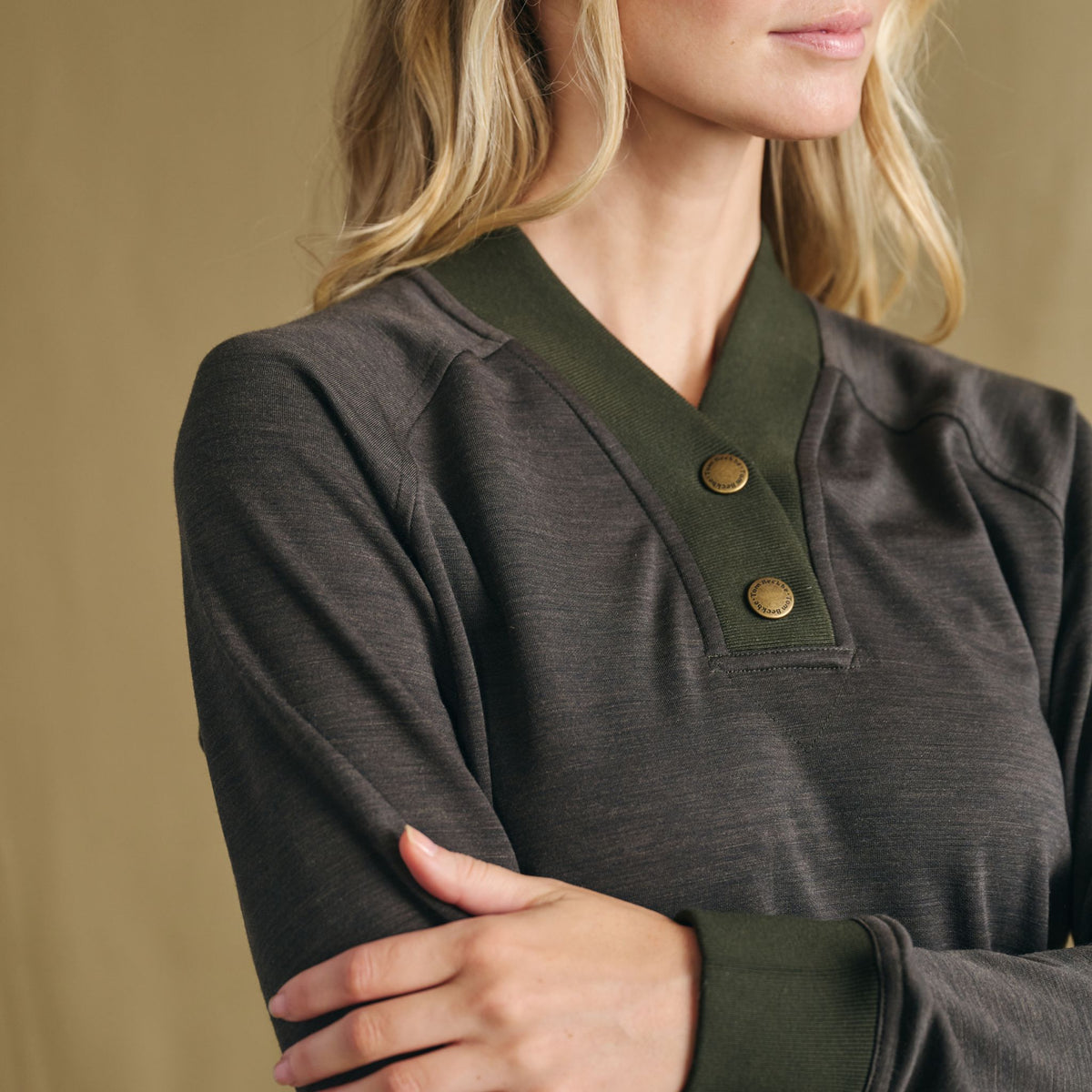Woman wears Tom Beckbe Women’s Shelby Fleece Pullover, arms crossed, in front of a plain beige background.