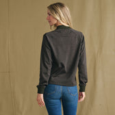 Woman models Tom Beckbe Women’s Shelby Fleece Pullover with blue jeans, facing away against a beige background.
