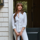Woman wears the Tom Beckbe Women's Tidewater Shirt, white plaid and lightweight, standing by a half-open door with a brown bag.