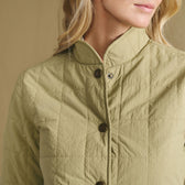 A close-up of a woman in the Tom Beckbe Women’s Tyler Quilted Jacket, light olive, with snap buttons, facing right.