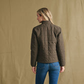 Person stands with back to camera, wearing Tom Beckbe Women’s Tyler Quilted Jacket and blue jeans.