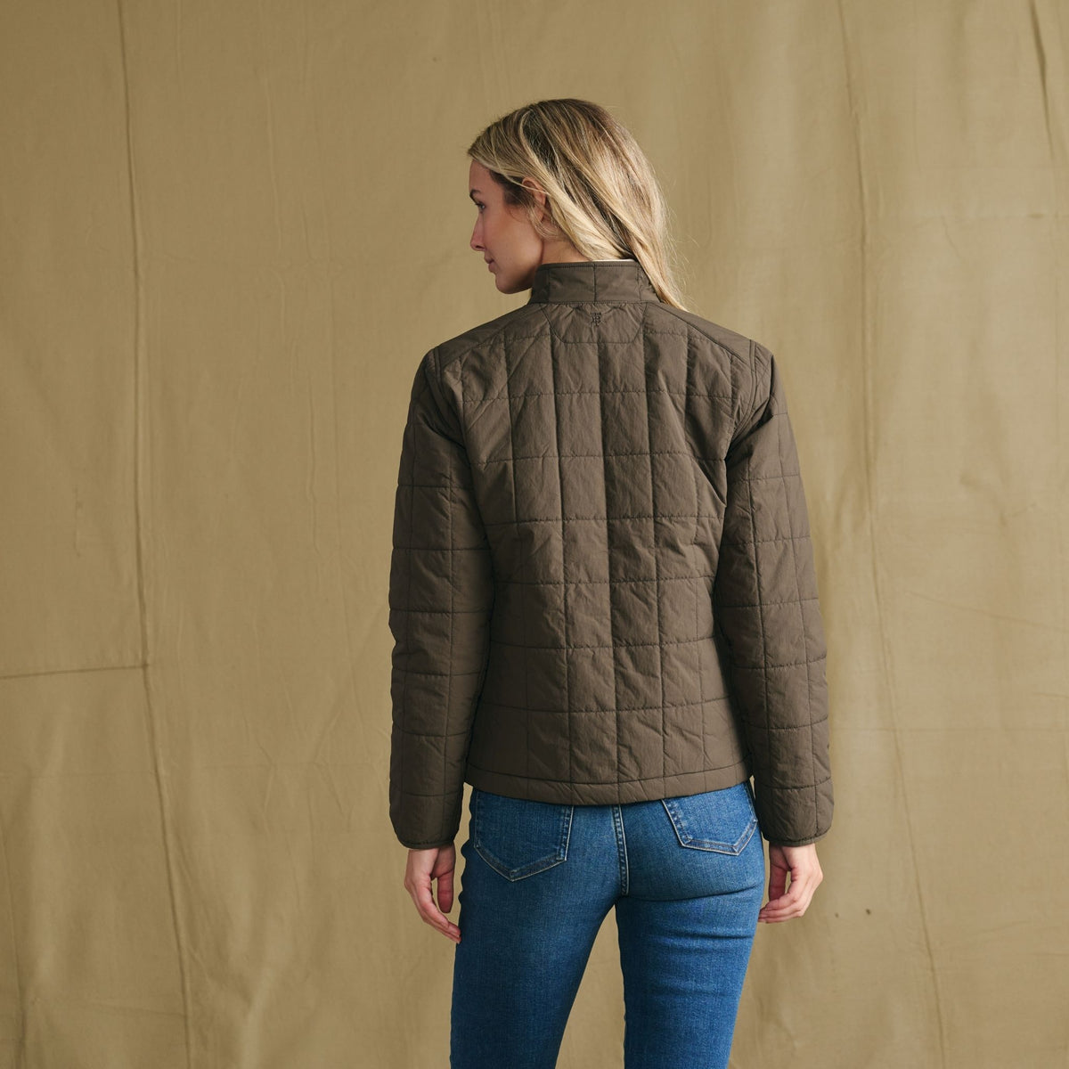Person stands with back to camera, wearing Tom Beckbe Women’s Tyler Quilted Jacket and blue jeans.