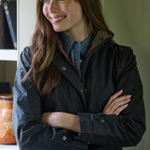 Woman with long brown hair wearing a dark jacket and blue shirt, standing with arms crossed and smiling.