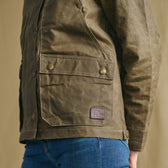 Woman in a Tom Beckbe Women’s Steward Jacket with buttoned pockets and blue jeans, shown from the side.