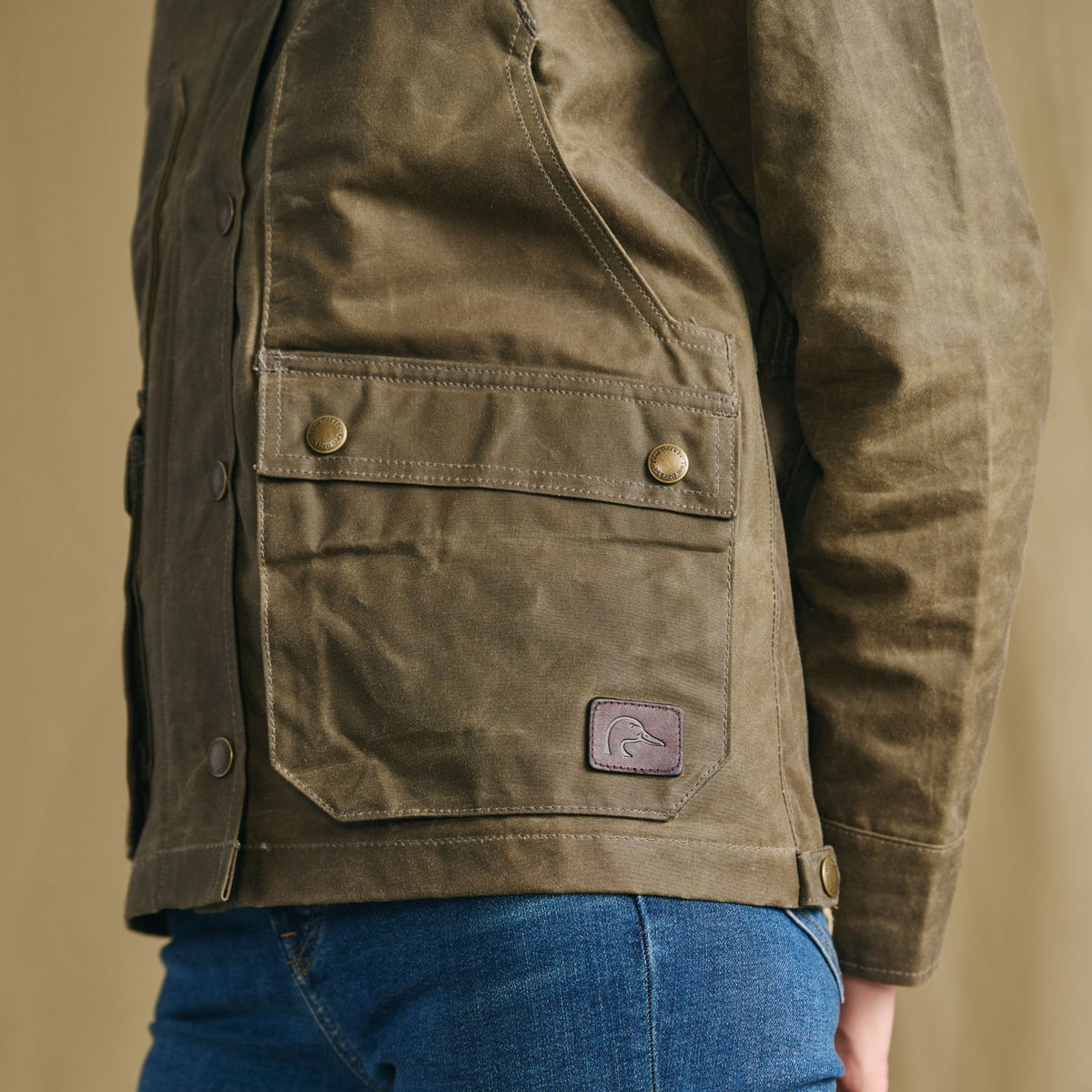Woman in a Tom Beckbe Women’s Steward Jacket with buttoned pockets and blue jeans, shown from the side.