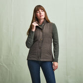 Woman in Tom Beckbe Womens Tyler Quilted Vest over a sweater and jeans, standing against a plain light backdrop.