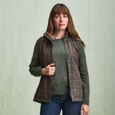 Woman wearing the Tom Beckbe Womens Tyler Quilted Vest over a green sweater and jeans, against a light background.