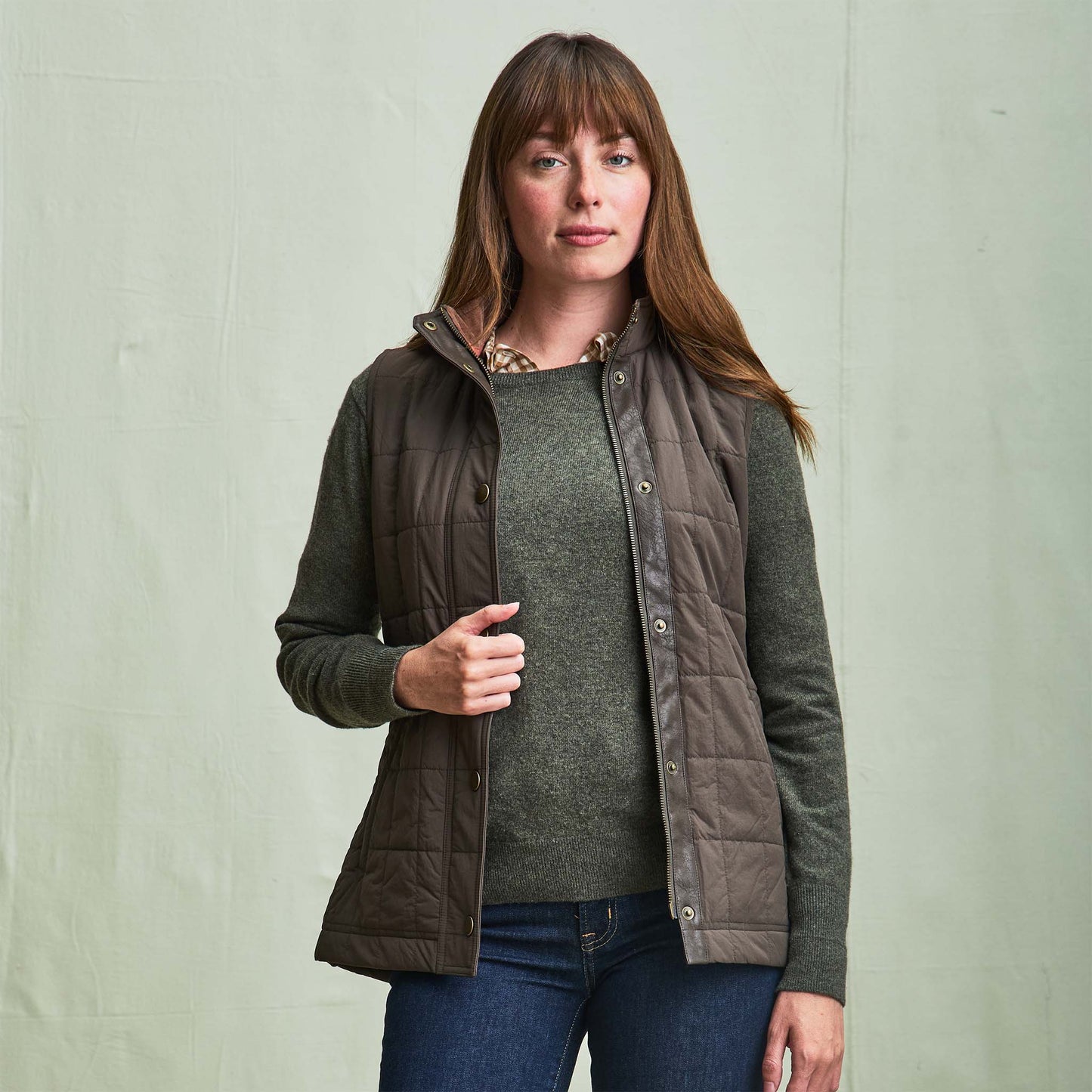 Woman wearing the Tom Beckbe Womens Tyler Quilted Vest over a green sweater and jeans, against a light background.