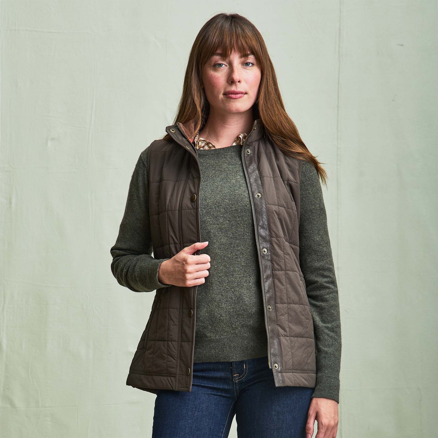 Woman wearing the Tom Beckbe Womens Tyler Quilted Vest over a green sweater and jeans, against a light background.