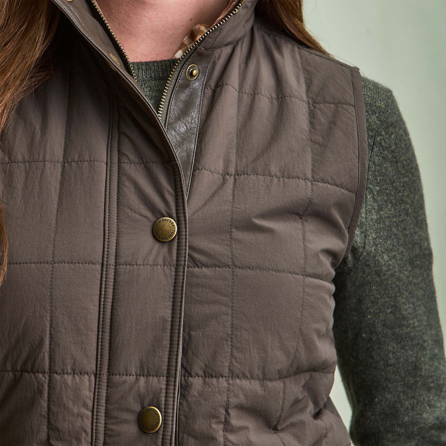 Close-up of a person wearing Tom Beckbe’s Womens Tyler Quilted Vest over a green knit sweater.