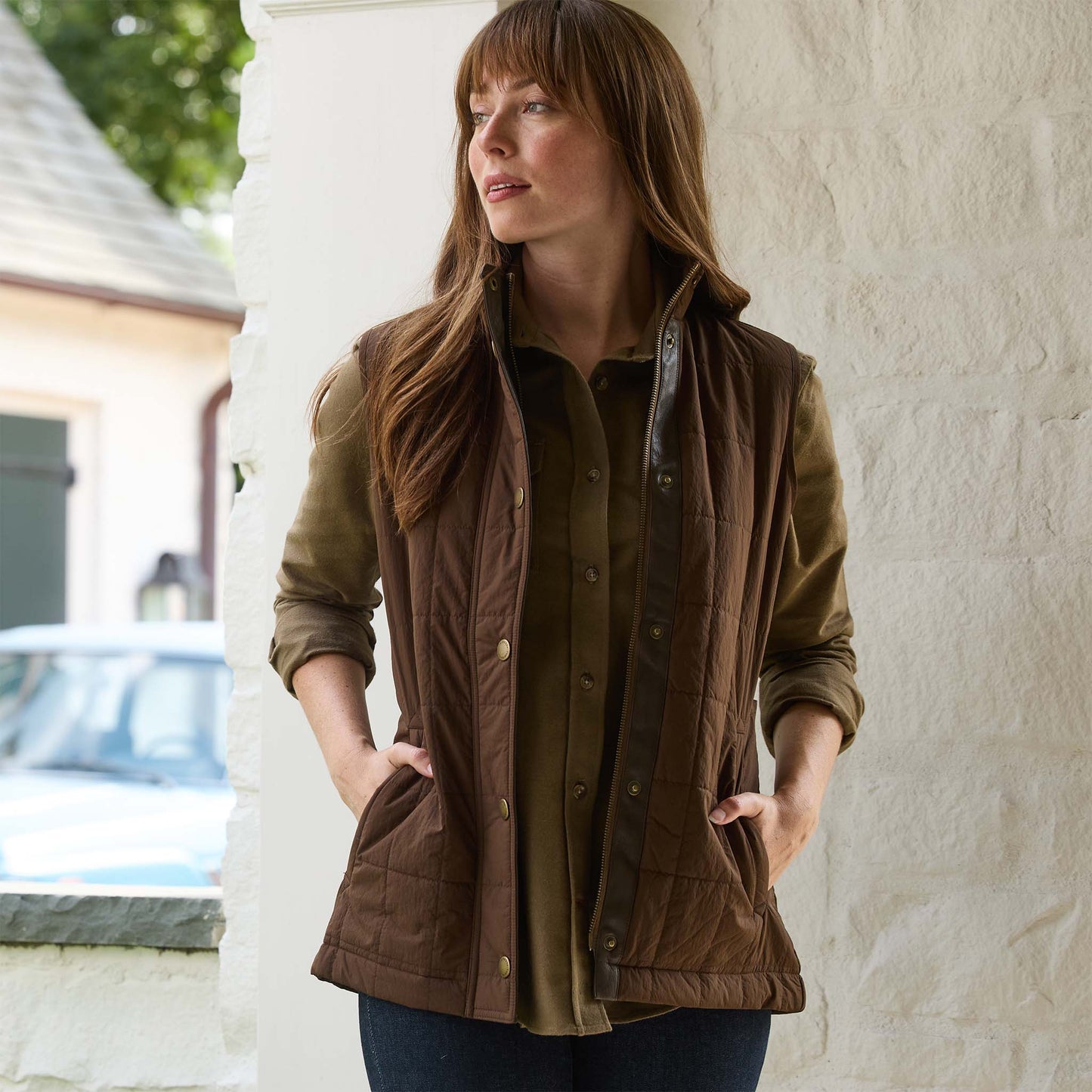 A woman outside, hands in pockets, wears the Tom Beckbe Womens Tyler Quilted Vest over a green shirt.
