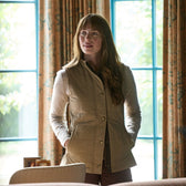 Woman with long hair wears the Tom Beckbe Womens Tyler Quilted Vest, standing indoors by a sunlit window with patterned curtains.