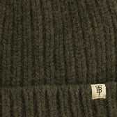 Close-up of Tom Beckbe's Wool Cap in ribbed dark green lambswool with a small beige TB tag.
