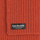 Close-up of an orange Tom Beckbe Wool Scarf with black label, made in the United Kingdom.