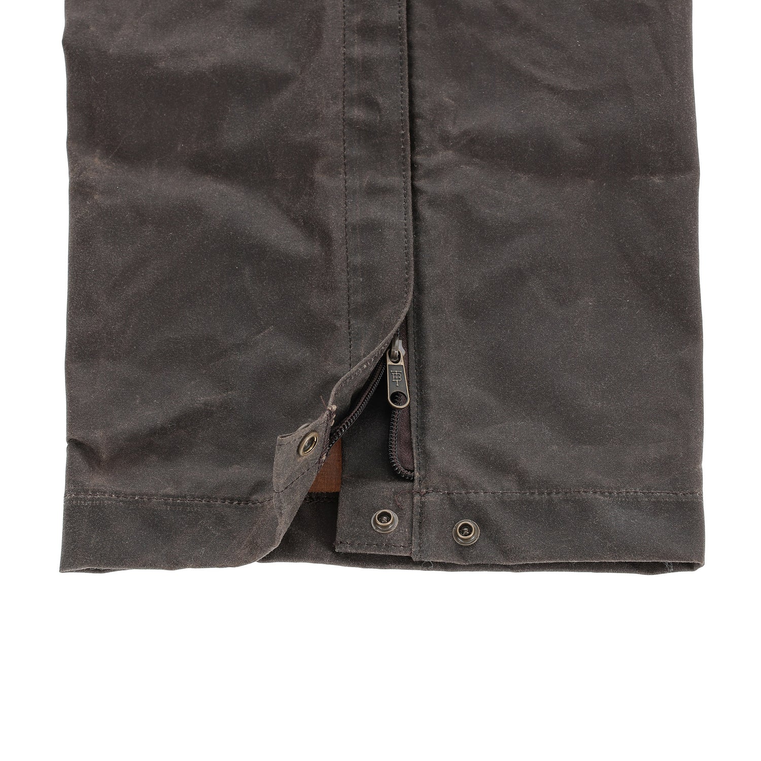Close-up of the Tom Beckbe Waxed Canvas Chaps hem with zipper and snap button closures.