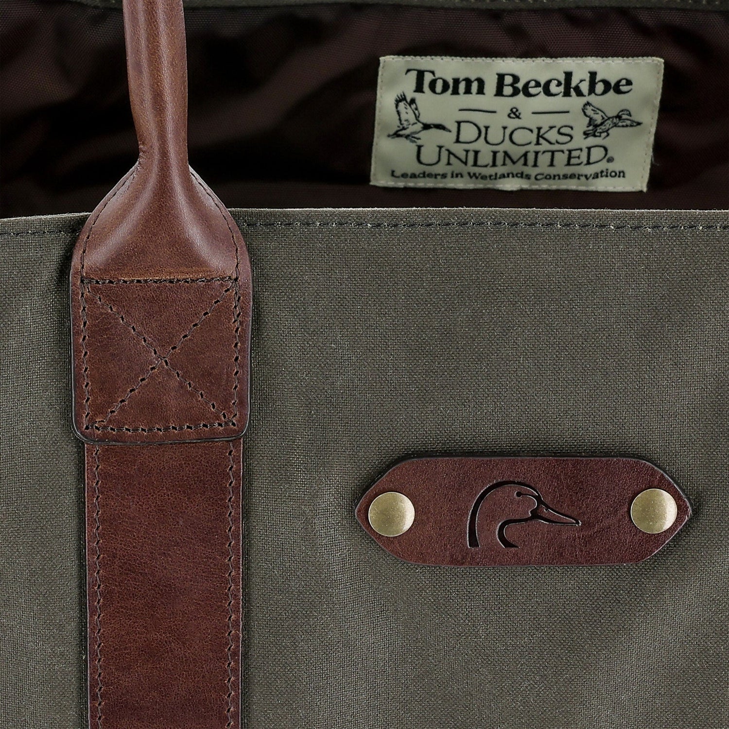 A close-up of the DU Canvas Carryall by Tom Beckbe, featuring leather straps and a Ducks Unlimited label.