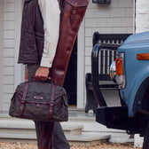 A person holds a Tom Beckbe DU Canvas Field Bag by a blue vehicle and white house.