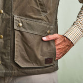 A person in a Tom Beckbe DU Kinsman Vest with snap buttons and a plaid shirt rests a hand in the large front pocket.