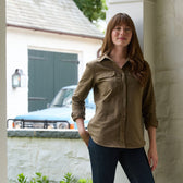 A woman in a Tom Beckbe Womens Mackay Moleskin Shirt and jeans stands by a white pillar with a blue car behind her.