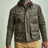 Man wearing a brown waxed jacket with large front pockets and khaki pants, shown from shoulders to mid-thigh.