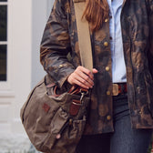 Person wearing a camouflage jacket and jeans carrying the Tom Beckbe DU Canvas Utility Bag with leather accents.