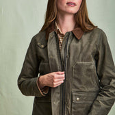 A woman zips up a green Tom Beckbe Womens Steward Jacket with brown collar; background is plain light green.