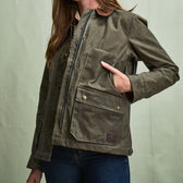 Person wearing a Tom Beckbe Womens Steward Jacket in olive green with snap buttons and front pockets.