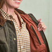 A person opens a dark green jacket to show an orange inner lining and an inner zippered pocket, wearing a checkered shirt.