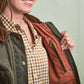 A person opens a dark green jacket to show an orange inner lining and an inner zippered pocket, wearing a checkered shirt.