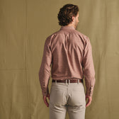Man standing with back to camera, wearing a checked long-sleeve shirt and light-colored pants against a plain backdrop.