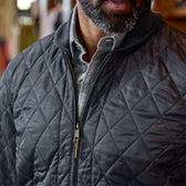 Man wearing a gray quilted jacket over a collared shirt; only lower face, neck, and torso are visible.