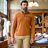 A man indoors wears the Tom Beckbe Tucker Fleece Quarter Zip in brown with khaki pants at a clothing store.