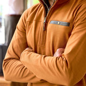 Person wearing a Tom Beckbe Tucker Fleece Quarter Zip in orange, arms crossed indoors; upper body shown, face not visible.