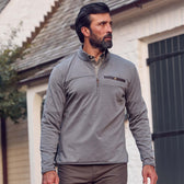 A bearded man wears a gray Tom Beckbe Tucker Fleece Quarter Zip outdoors near a white building with a dark door.