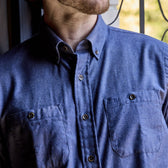 A person wears a Tom Beckbe Dixon Brushed Cotton Twill Shirt with two chest pockets, standing by a window.