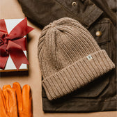 A Tom Beckbe Wool Cap, brown jacket, orange gloves, and gift box with red bow create a classic look on a tan surface.