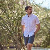 Man wearing a Tidewater Shirt by Tom Beckbe and shorts, strolls outside with trees in the background.