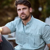 Man with short hair and beard wearing a Tom Beckbe Tidewater Shirt, UPF 30+, sits outdoors neutrally.