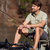Man smiling on a boat, holding a rod, wearing Tom Beckbes Tidewater Shirt and shorts.