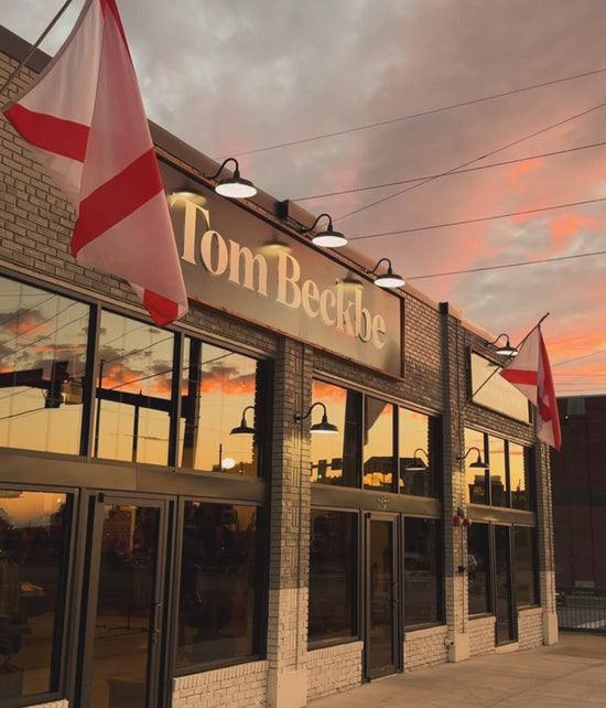 Building exterior with Tom Beckbe sign, displaying red and white flags, under a colorful sunset sky.