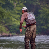 Fly fisherman casting a fly rod on a stream wearing an all-weather ripstop fishing hip pack.