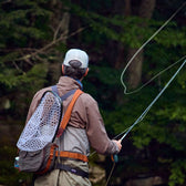 Fly fisherman casting a fly rod on a stream wearing a fishing hip pack and mesh fishing net.