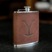 Tom Beckbes Yellowstone Hip Flask, 6oz brown leather with silver, embossed Y, on a black surface.